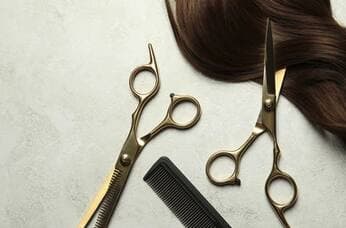 Hairdressing scissors and a comb beside a section of brown hair