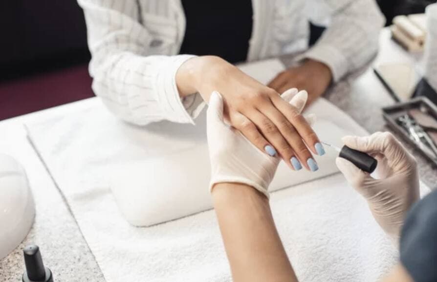 A nail technician painting light blue polish on a client's nails
