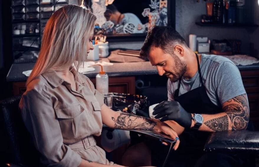 A tattoo artist working on a client's forearm in a studio